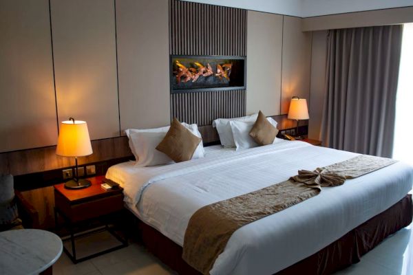 A modern hotel room with a large bed, decorative pillows, two bedside lamps, and a small table, featuring warm lighting and neutral tones.