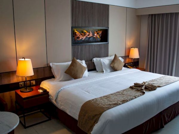 A modern hotel room with a large bed, decorative pillows, two bedside lamps, and a small table, featuring warm lighting and neutral tones.