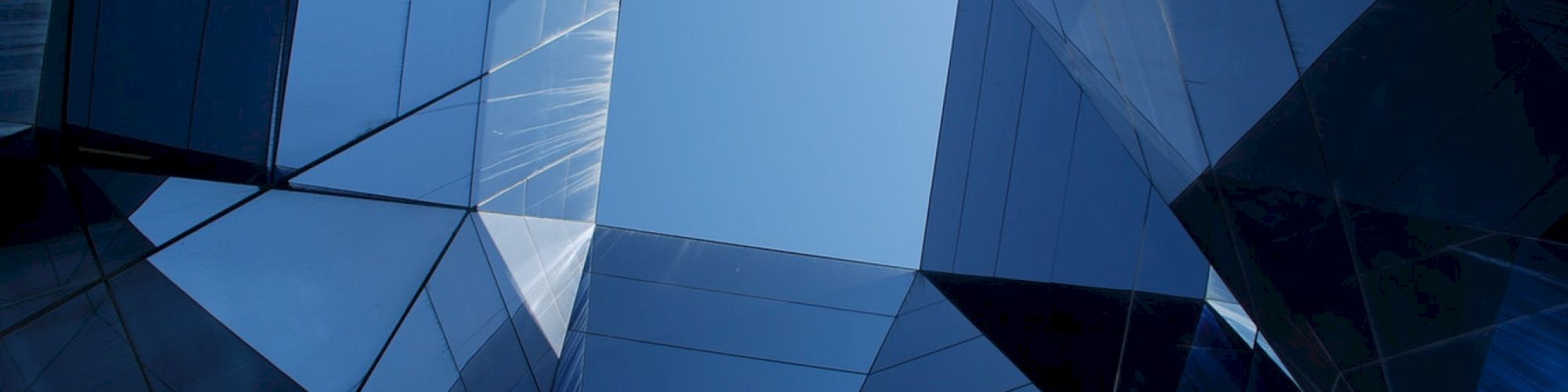 Abstract architectural structure with reflective glass surfaces creating a geometric pattern against a blue sky.