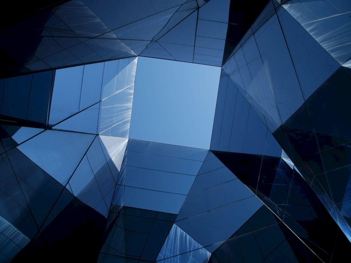 Geometric glass structures form a pattern with reflective surfaces, creating an open skylight view in the center.