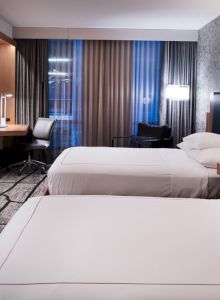 This image shows a modern hotel room with two beds, a flat-screen TV, a desk, and patterned wallpaper, creating a cozy atmosphere.