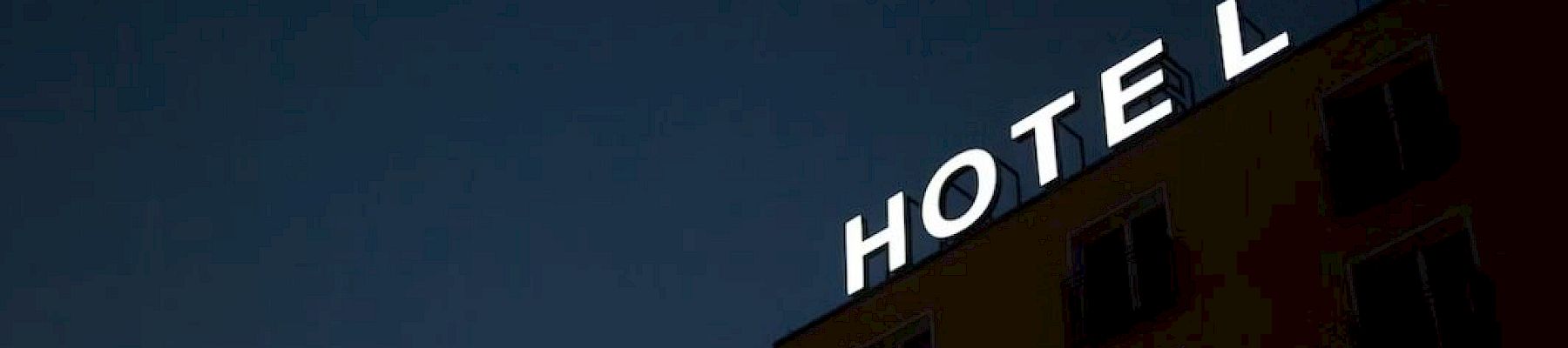 The image shows a building with illuminated letters spelling "HOTEL," but the letter "L" is partially missing or obscured, against a dark sky.