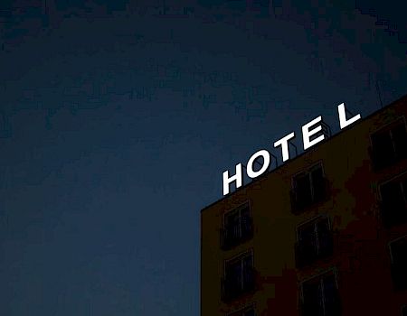 The image shows a building with illuminated letters spelling "HOTEL," but the letter "L" is partially missing or obscured, against a dark sky.