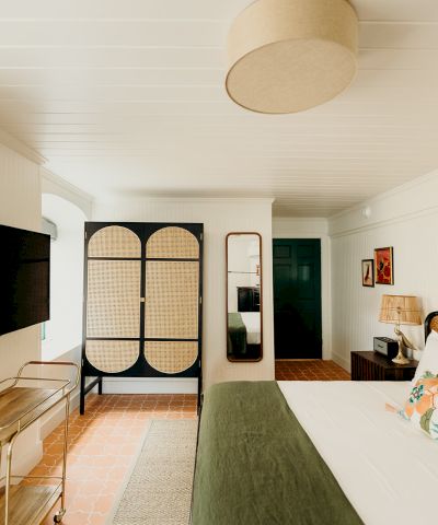 A cozy bedroom with a bed, TV, stylish screen, mirror, and decor accents. Neutral and green tones create a calming atmosphere.