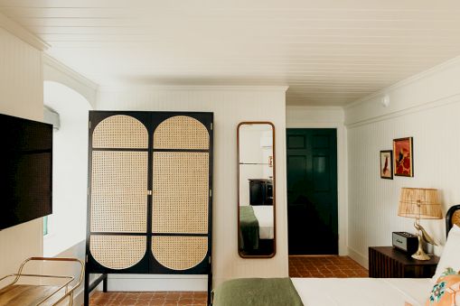 A cozy bedroom with a bed, TV, stylish screen, mirror, and decor accents. Neutral and green tones create a calming atmosphere.