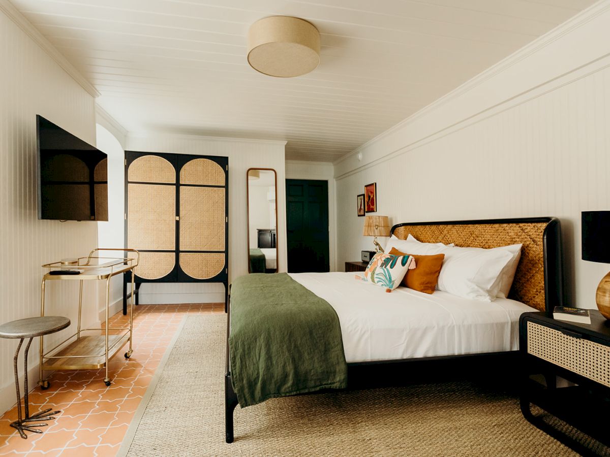 A stylish bedroom with a bed, green throw, wall-mounted TV, and unique furniture, featuring warm tones and modern decor elements.