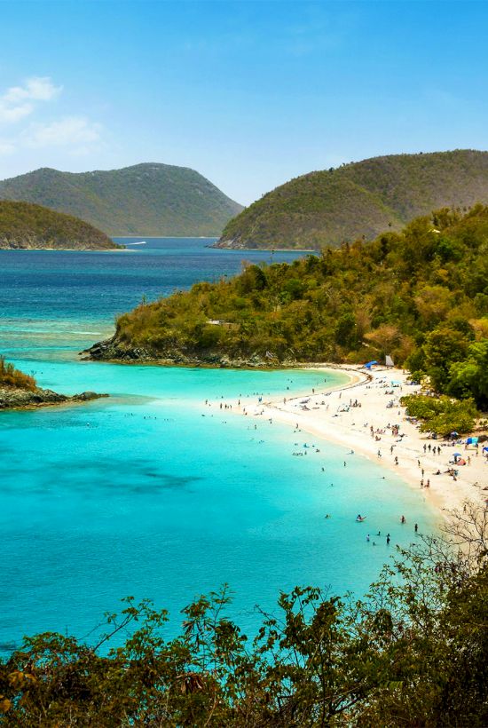 A scenic view of a tropical beach with clear turquoise waters, surrounded by green hills and scattered islands in the background.