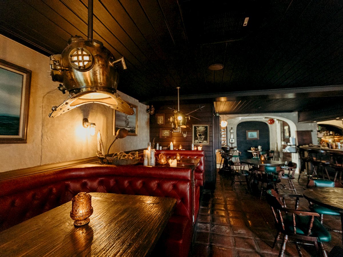 A cozy pub or restaurant with wooden tables, vintage decor including a diving helmet, leather seating, warm lighting, and nautical theme.