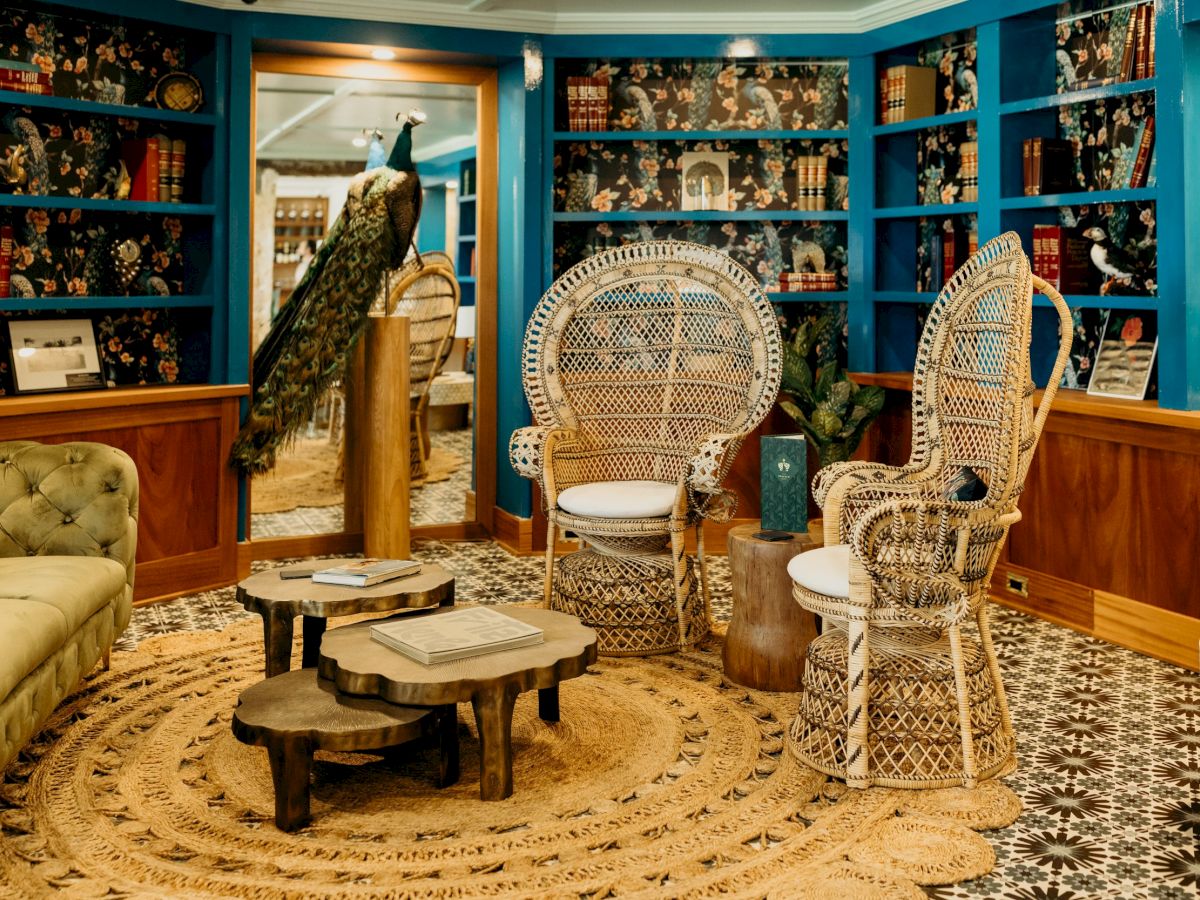 A cozy room with wicker chairs, a peacock statue, bookshelves, and a circular rug, creating an inviting and artistic atmosphere.