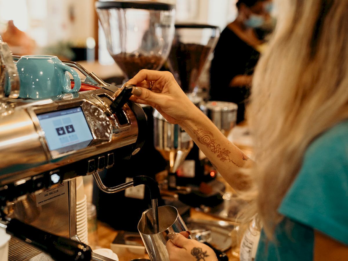 A barista operates an espresso machine in a coffee shop, surrounded by coffee equipment and focused on preparing a drink.