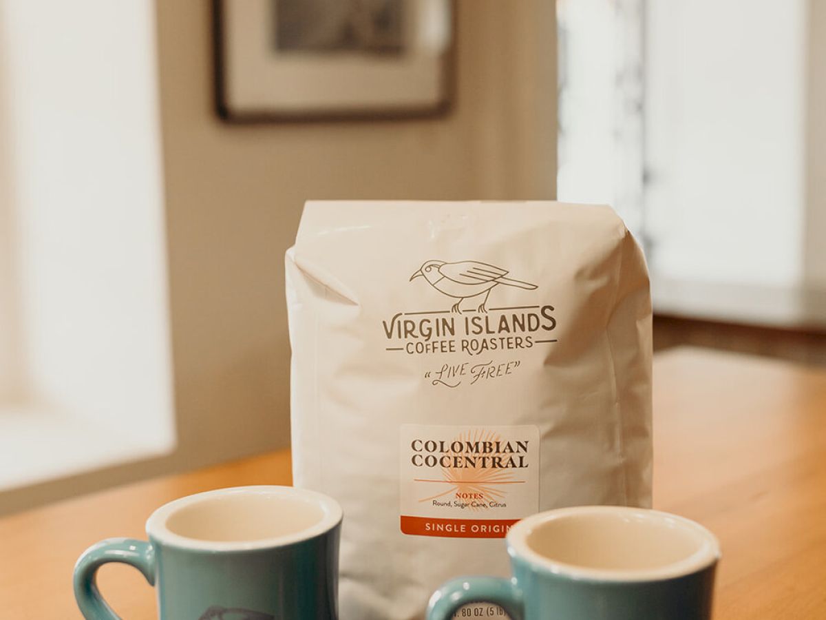 Two blue mugs and a bag of Caribbean Reserve coffee on a wooden table, with a blurred background.