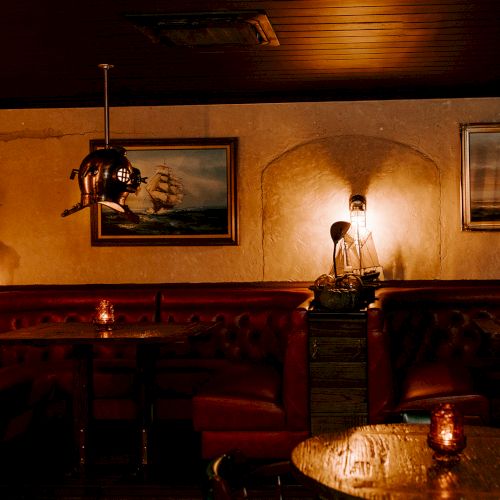 A dimly lit, cozy pub or bar with red booth seating, nautical-themed decor, and warm ambient lighting ending the sentence.