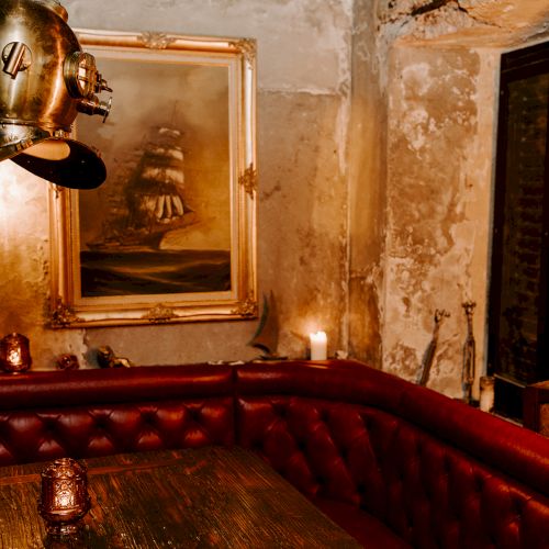 A vintage-themed room with a diving helmet, ship painting, red tufted seating, and warm lighting creates a cozy atmosphere.