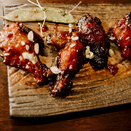 Grilled chicken wings garnished with sliced almonds on a wooden plate, accompanied by a green garnish and a red napkin.