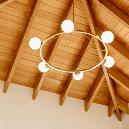 A wooden vaulted ceiling with exposed beams features a circular chandelier with six round lights.