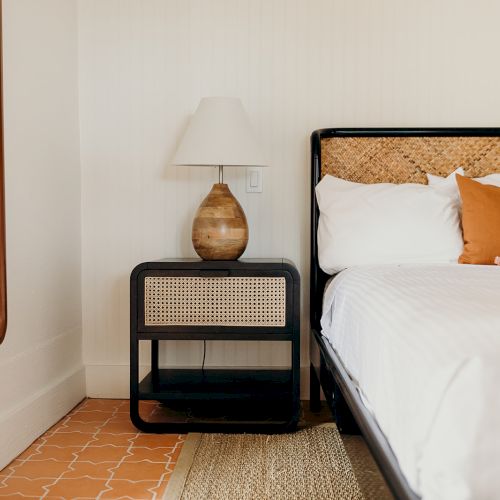 A cozy bedroom corner with a bed, patterned pillows, a nightstand, a ceramic lamp, and a large mirror on the wall.