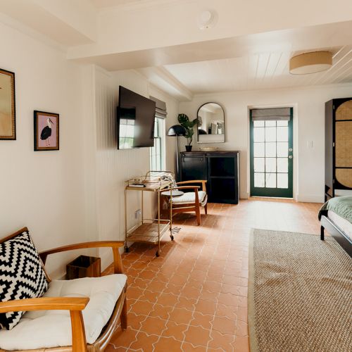 This image shows a cozy bedroom with a chair, a bed, a TV, artwork, and a large wardrobe in a bright, spacious setting.
