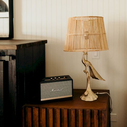 A cozy bedroom scene with a wicker lamp, vintage-style radio, dark cabinet, and a woven headboard, creating a warm, rustic vibe.