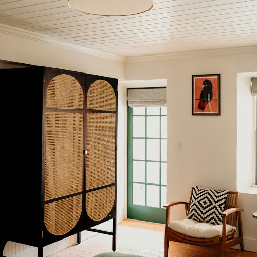 A cozy bedroom with a modern light fixture, a patterned chair, a minimalist wardrobe, and a framed artwork on the wall.
