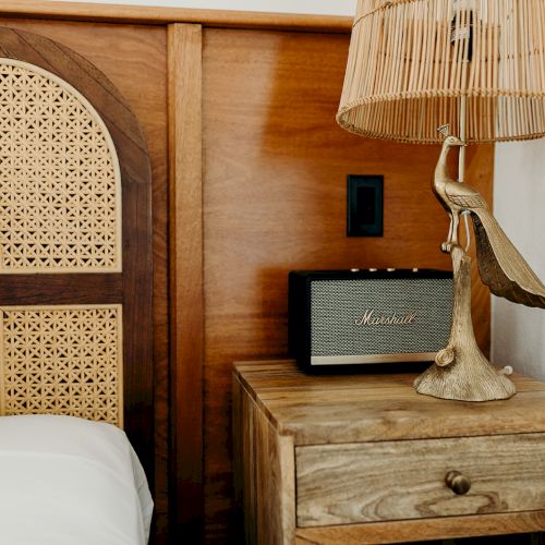 A cozy bedroom scene with a wooden headboard, a vintage-style lamp, and a small speaker on a bedside table.