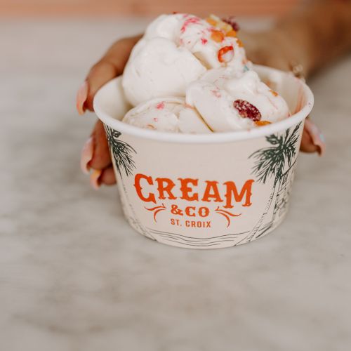 A person is holding a cup of ice cream with the label "Cream & Co St. Croix" on it.
