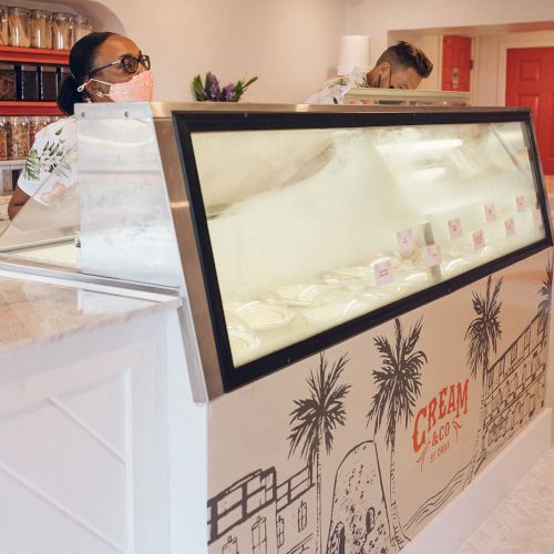 An ice cream shop interior with a display counter and two people standing behind it.