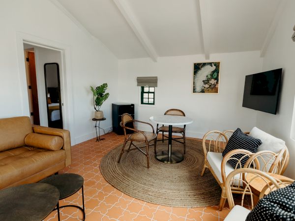 A cozy living room with a brown couch, wicker chairs, table, TV, and decor on terracotta tile flooring.
