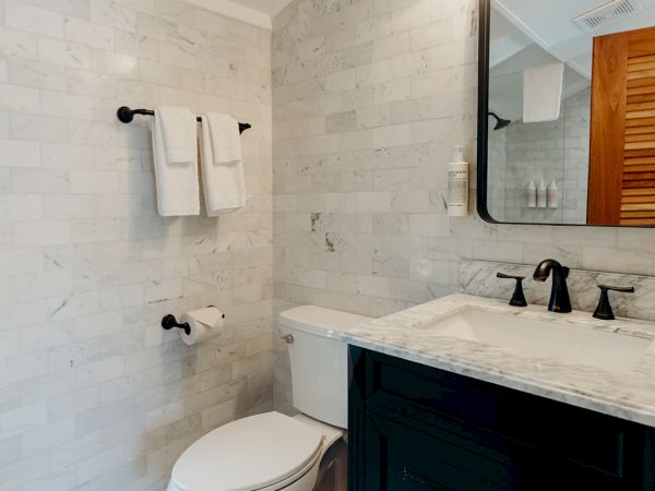 A modern bathroom with a toilet, marble countertop, black vanity, mirror, towel rack, and decorative floor tiles.