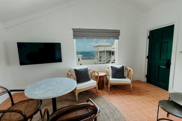 A cozy room with a TV, round table, chairs, and a view of the ocean through a window.