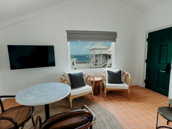 A cozy room with a TV, round table, chairs, and a view of the ocean through a window.