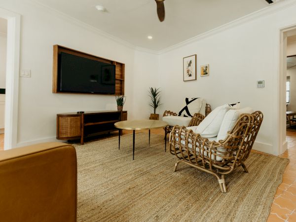 A cozy living room with wicker chairs, a round coffee table, a TV on the wall, and decor, featuring a neutral color scheme and woven rug.