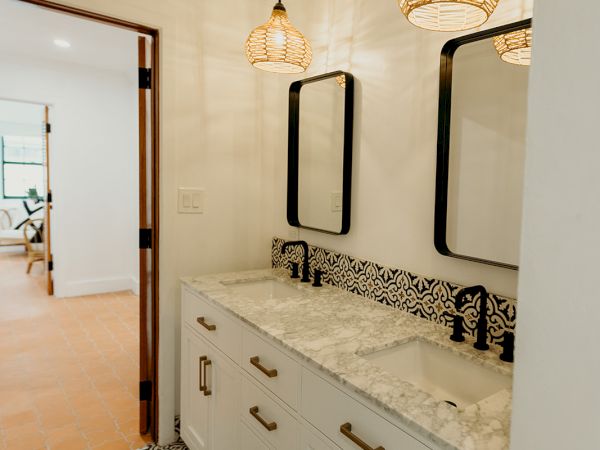 A bathroom features patterned floor tiles, a double vanity with marble countertops, black fixtures, and pendant lights.