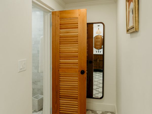 A small hallway with patterned floor tiles leads to a room with a wooden sliding door. A mirror and a framed picture are on the walls.