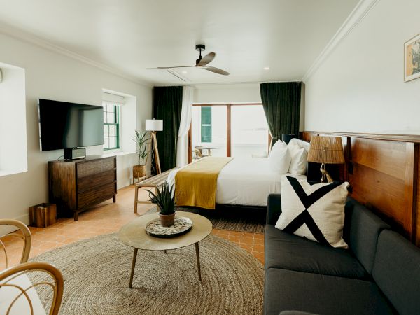 The image shows a modern bedroom with a bed, sofa, TV, wooden furniture, and a coffee table, creating a cozy, stylish atmosphere.