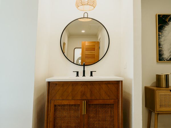The image shows a bathroom vanity with a round mirror and a wooden cabinet, under a pendant light, on patterned tile flooring.