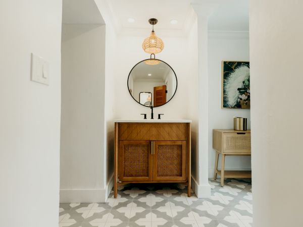 A stylish bathroom featuring a wooden vanity with a round mirror, geometric floor tiles, and modern lighting.
