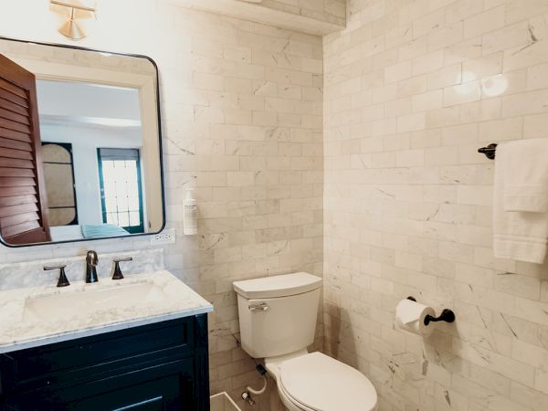 The image shows a bathroom with a toilet, a vanity with a mirror, a towel rack, and ornate floor tiles.