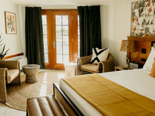 A cozy room with a double bed, wicker chairs, a round table, and a patterned accent wall. French doors open to the outside.