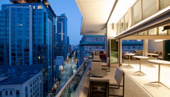 Modern rooftop patio with tables and chairs overlooking an urban cityscape at dusk.