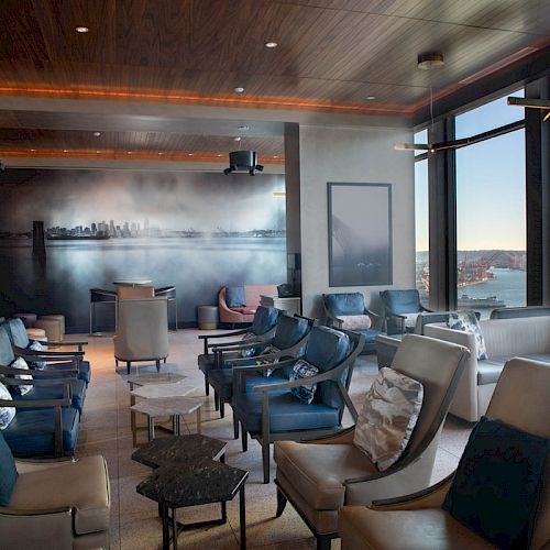 A modern lounge with plush seating, wall art, and large windows showcasing a waterfront view with a Ferris wheel in the distance.