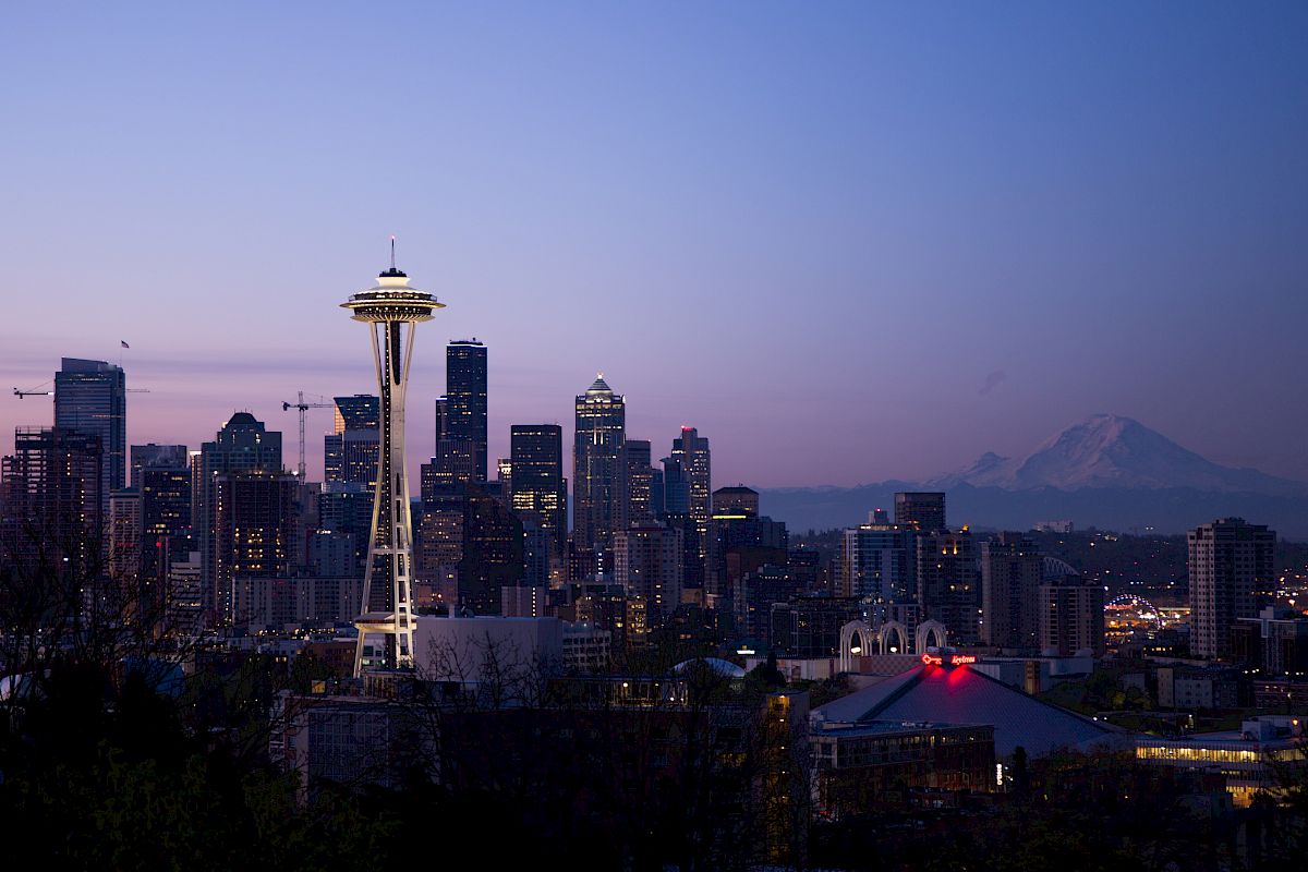 The image shows the Seattle skyline at dusk, featuring the Space Needle and Mount Rainier in the background.