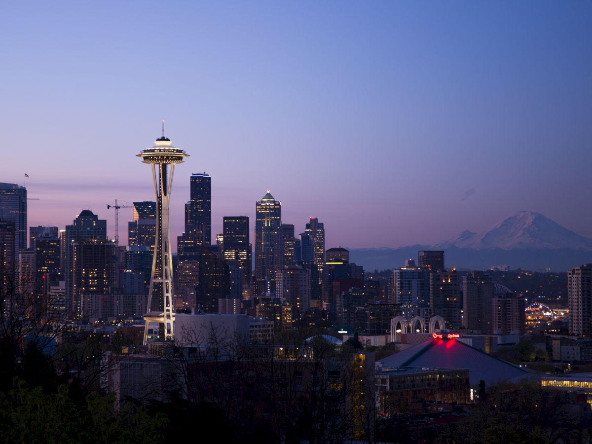 The image shows the Seattle skyline at dusk, featuring the Space Needle and Mount Rainier in the background.
