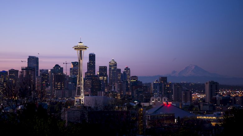 The image shows the Seattle skyline at dusk, featuring the Space Needle and Mount Rainier in the background.