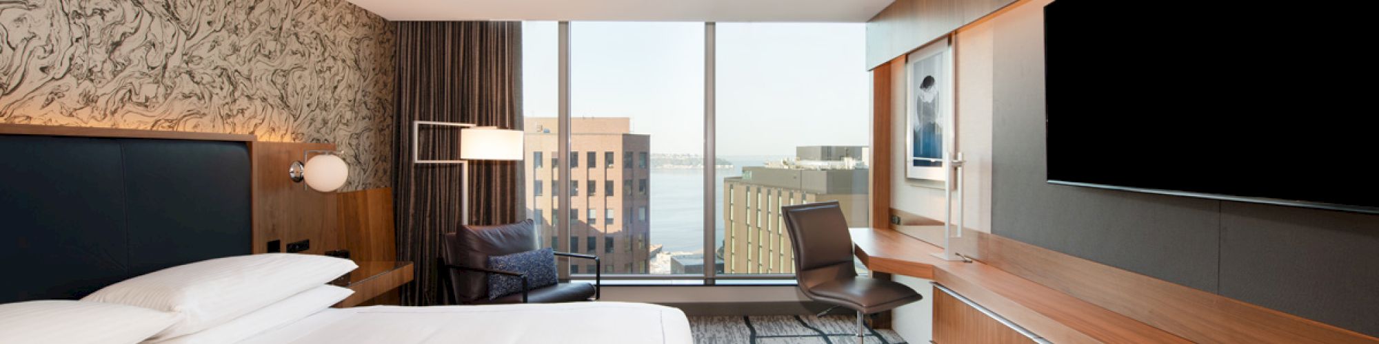 A modern hotel room with a bed, desk, large TV, and view of city buildings through a window completes the scene.